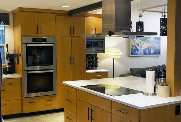 Maple cabinets, double wall ovens and a white quartz island with cooktop under a stainless hood in a Seattle kitchen