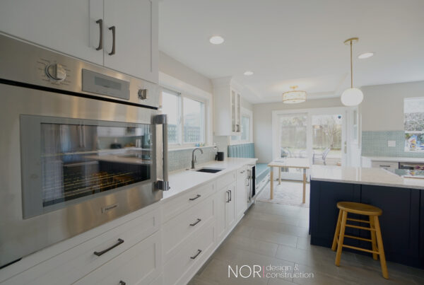 Stainless wall oven and white cabinets leading to a navy island in a bright Seattle kitchen remodel