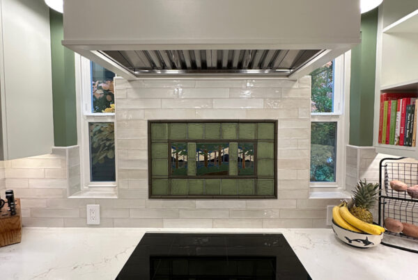 Painted range hood above a cooktop and framed tile mural in a West Seattle kitchen remodel
